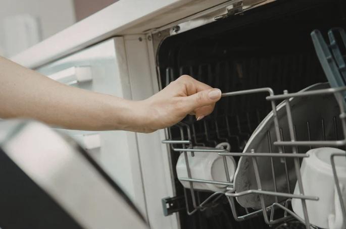 hand pulling on the top rack of a dishwasher