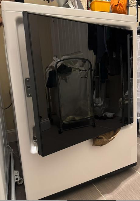 Front-load dryer in a New Jersey laundry room with the dark glass door partially open and clothing visible at the bottom, used to show issues that may require local appliance repair.
